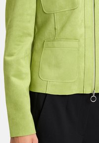 Zielona zamszowa kurtka z dwoma przednimi kieszeniami, z zapięciem na zamek oraz metalowym detalem w dolnej części. Posiada dopasowany krój i miękką teksturę.