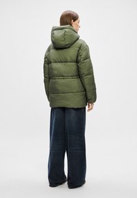 Giacca a vento verde con cappuccio, caratterizzata da un design trapuntato e una vestibilità comoda. Abbinata a jeans in denim scuro a gamba larga.