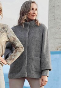 Grauer, gestrickter Pullover mit hohem Kragen, weiten Ärmeln und zwei vorderen Taschen. Strukturiertes Material mit einem leicht übergroßen Schnitt.