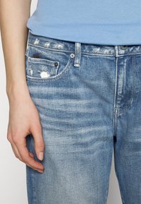 Ljust blå denimjeans med en sliten finish, featuring revor, fickor och silverfärgad hårdvara på midjan.