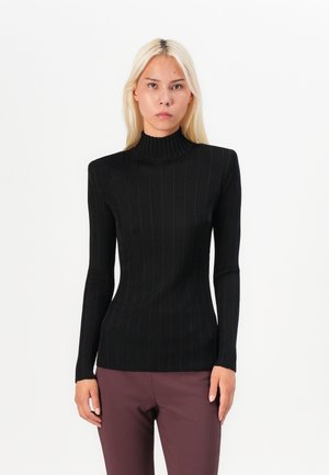 Black ribbed turtleneck made of fitted stretch fabric, featuring long sleeves and a high neckline, paired with dark trousers.