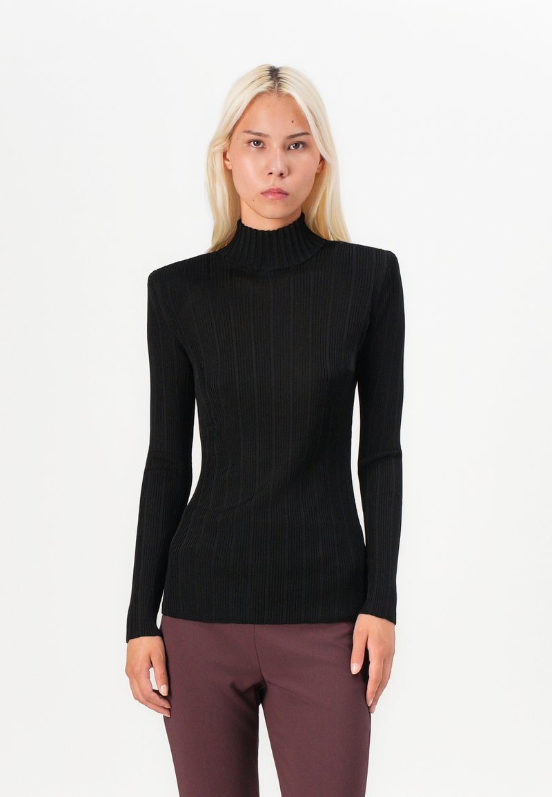 Black ribbed turtleneck made of fitted stretch fabric, featuring long sleeves and a high neckline, paired with dark trousers.