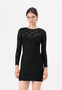 Robe noire à manches longues en dentelle texturée, mettant en avant une silhouette ajustée et un motif floral. Tissu lisse et col montant.