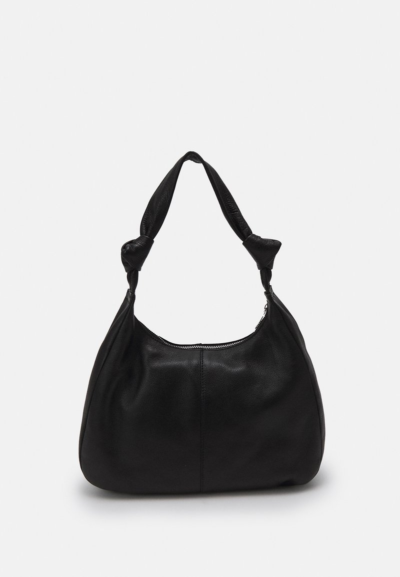 Sac à bandoulière en cuir noir avec sangle nouée et fermeture éclair supérieure sur un fond uni gris clair.