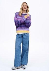 Sveter: fialový gradientný úplet so žltým lemom; široké, dlhé rukávy. Džínsy: svetlomodré, voľný strih. Topánky: biele a sivé tenisky.