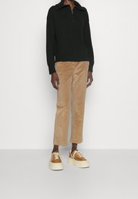 Suéter negro con cremallera en el cuello, pantalones de pana beige y zapatillas de plataforma marrón claro con suelas en blanco roto. Diseño ajustado con puños y cuello acanalados.