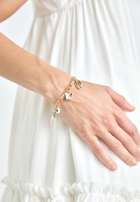 Gouden armband met een gemengd kettingontwerp, versierd met bedels waaronder een schelp, vlinder, blauwe kraal en vis.