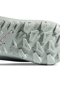 Semelle de chaussure en caoutchouc gris clair avec des sculptures géométriques profondes et de petites taches sombres, présentant le logo Michelin proche du talon.