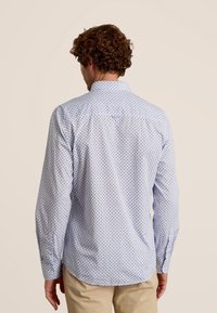 Lange mouwen shirt in lichtblauw met een geometrisch patroon. Zachte stof, puntkraag, met knopen afsluitbare manchetten en een afgeronde zoom aan de achterkant.