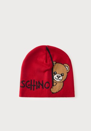 Rote gestrickte Mütze mit einem lächelnden Teddybär, der von der Seite hervorschaut, und schwarzem Text, der vorne teilweise "MOSCHINO" buchstabiert.