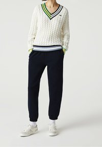 Vitrandig kabelstickad tröja med V-hals och gröna, marinblå och blå ränder. Marinblå joggerbyxor med elastiska ärmslut och vita sneakers.