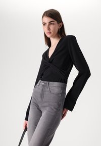 Juoda ilgomis rankovėmis palaidinė su sukta priekiu, derinama su aukštu juosmeniu pilkais džinsais, turinčiais klasikinę penkių kišenių išvaizdą.