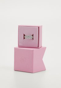 Bague argent large ornée de plusieurs petits diamants, présentée dans une boîte à anneau en velours rose avec un logo embossé à l'extérieur.