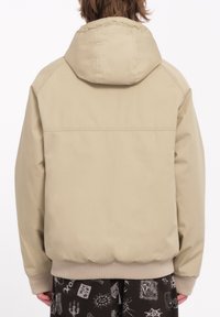 Beige hættetrøje med en glat tekstur, elastiske manchetter og nederste kant samt et simpelt design. Set bagfra, uden yderligere detaljer.