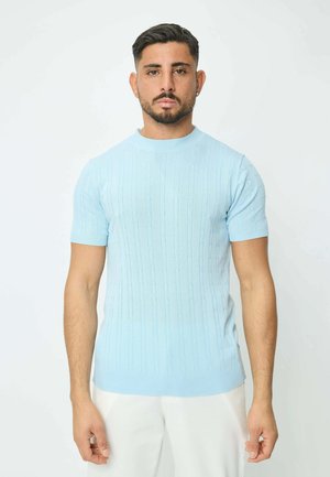 Pull en maille bleu clair à manches courtes avec texture côtelée et délicates rayures verticales, associé à un pantalon blanc.