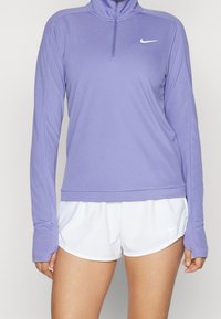 Ljuslila långärmad träningsskjorta med halvdragkedja och vit Nike-logotyp. Tillsammans med vita shorts som har en diskret Nike-logotyp.