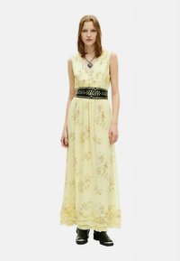 Maximekko vaaleankeltaisesta kankaasta, jossa on kukkakuvioita. Siinä on musta niitillinen vyö, liehuva helma ja V-kaula-aukko.