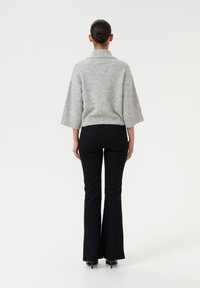 Maglione grigio a trecce con colletto alto, maniche ampie e vita aderente. Abbinato a jeans neri a zampa d'elefante, che mettono in risalto una texture liscia.