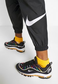 Svarta Nike-sneakers med färgglada, randiga detaljer och vitt märke. I kombination med prydligt avskurna svarta byxor med ett stort vitt märke.