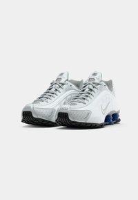 Pair of white and gray Nike Shox sneakers with blue cushioning and black soles, viewed from front-left angle on white background.