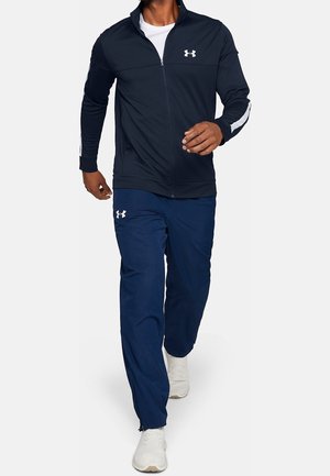 Marineblaue Zip-up-Jacke mit weißen Akzenten und Logo, kombiniert mit passenden marineblauen Hosen. Aus leichtem Stoff gefertigt, für aktive Aktivitäten konzipiert.