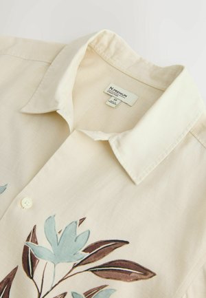 Cămașă cu mâneci scurte de culoare crem, cu guler, decorată cu broderie florală albastră și maro. Include închidere cu nasturi albi și etichetă de întreținere.