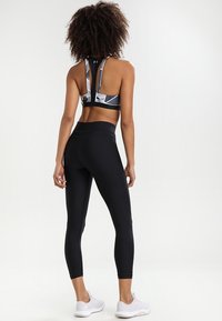 Černé legíny a vzorovaná sportovní podprsenka s geometrickými vzory, která má styl racerback. Textura je hladká a přiléhavá.