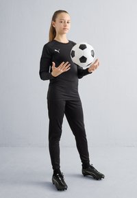 Zwarte sportoutfit bestaande uit een shirt met lange mouwen en een broek, met een zwarte en witte voetbal, gedragen met zwarte voetbalschoenen.
