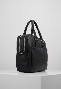 Schwarze Lederhandtasche mit strukturierter Oberfläche, doppelten Tragegriffen, einem Reißverschluss oben und einer Fronttasche, die durch Metallbeschläge akzentuiert wird.