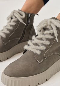 Graue Wildlederstiefeletten mit dicken, strukturierten grauen Schnürsenkeln, seitlichem Reißverschluss und einer klobigen, hellgrauen Sohle mit vertikalen Rillen.