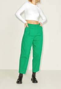 Gröna, högmidjade byxor med framfickor, i kombination med en vit kortärmad topp och svarta snörskor.