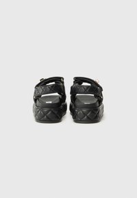 Sandales noires matelassées avec des sangles rembourrées et une semelle épaisse. Présente des accents en matériel doré et un doublure intérieure lisse pour le confort.