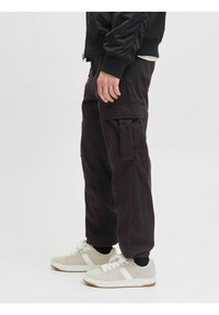 Schwarze Cargo-Hosen mit mehreren Taschen, einem lockeren Schnitt und elastischen Bündchen, kombiniert mit hellen Sneakers. Glatte Stofftextur.