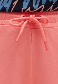 Korallenrote Sweatpants mit glatter Textur, ausgestattet mit einem Kordelzug mit Kunststoffenden und einem elastischen Bund. Das Oberteil ist marineblau mit buntem Text.