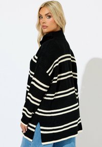Svart och vit randig stickad tröja med hög krage, sidofickor och en avslappnad passform. Texturerat tyg ger värme och komfort.