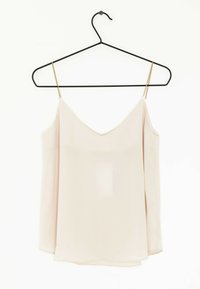 Top de camisón beige claro con diseño de escote en V, tirantes finos y una silueta fluida, colgando de una percha de metal negra contra un fondo blanco.
