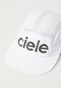 White cap featuring a smooth bill and textured mesh panels. The front displays a bold black "ciele" logo.