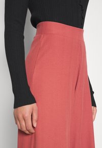 Roze geribde wijde broek met hoge taille. Een zwart langemouwen top is gedeeltelijk zichtbaar en toont het kleurcontrast.