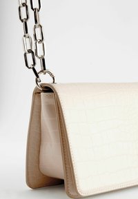 Sac à main beige clair avec une texture crocodile, présentant une forme structurée et une bandoulière en chaîne argentée brillante avec des maillons ovales.