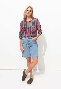 Chemise à carreaux avec des nuances de rose, vert et bleu, associée à un short en denim bleu clair. Des chaussures brunes à enfiler complètent la tenue.