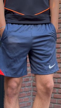 Calções desportivos azuis-marinho feitos de tecido que afasta o suor, com um logótipo branco da Nike e detalhes em laranja na cintura.