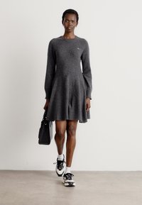 Abito grigio a maniche lunghe con gonna svasata, realizzato in un materiale morbido. Abbinato a sneaker nere e a una borsa nera.