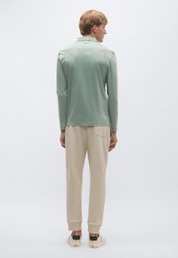 Hosszú ujjú, menta zöld póló egyenes szegéllyel, bézs melegítőnadrággal párosítva. Puha anyagból készült, kényelmes szabással.