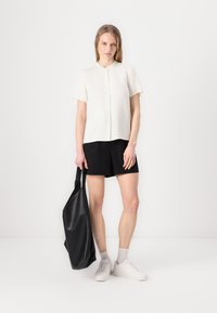 White short-sleeve button-up shirt, black shorts, and a large black textured tote bag. Model wears white sneakers and light gray socks.