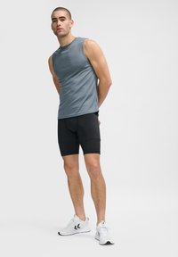 Grå ærmeløs træningsshirt kombineret med sorte shorts og hvide sneakers. Shirt er lavet af et glat materiale og har diskret branding.