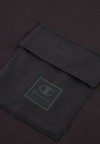 Sudadera Champion negra con un bolsillo con tapa, textura suave y un logotipo prominente en un cuadrado en el centro.