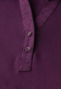 Violetti polo-paita, jossa on teksturoitu kangas, kaulus ja kolme samanlaista nappia, jossa on kukkakuosi koristeena.