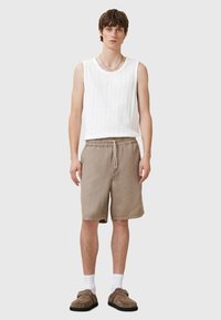 Vit ribbad linne kombinerat med beige shorts som har ett elastiskt midjeband. Modellen bär bruna slip-on skor med vita ankelsockor.