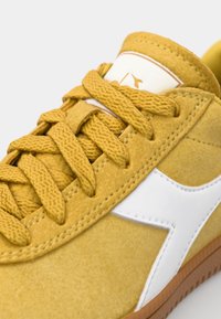 Yellow suede sneaker with white leather logo and lacing, featuring a textured surface and a gum rubber sole.