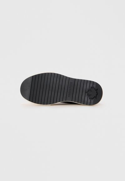 Semelle de chaussure en caoutchouc noir avec des nervures texturées. Présente un logo en forme de feuille et un bord de couleur claire. Surface lisse avec une finition mate.